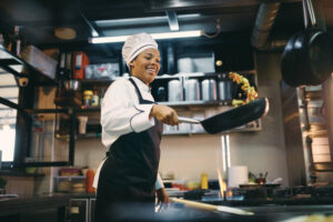 African American female chef having fun while preparing food in the kitchen at restaurant.